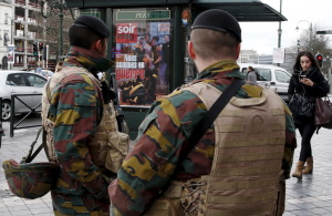 Belgian soldiers stand guard in front of a poster for Le Soir weekly news magazine, after security was tightened following the fatal attacks in Paris, in Brussels, Belgium